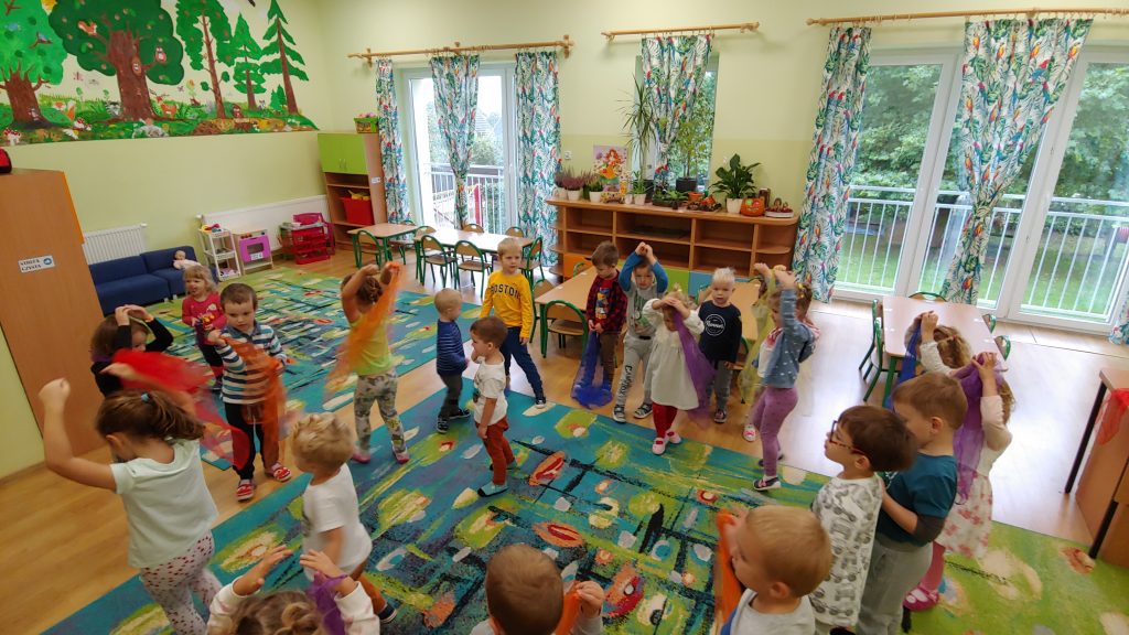 dzieci tańczą przy muzyce z kolorowymi tiulowymi chustami w ręku.