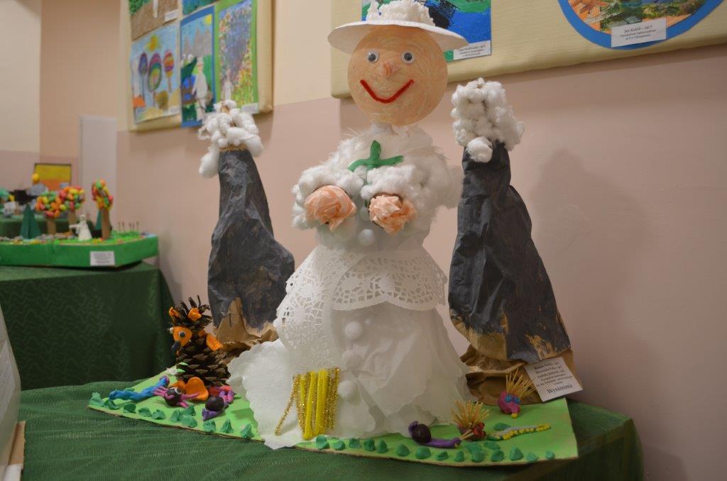 Postać Papieża wykonana z białego papieru, głowa z kuli styropianowej w kapeluszu, przy dwóch strzelistych papierowych górach, na tle prac w galerii.