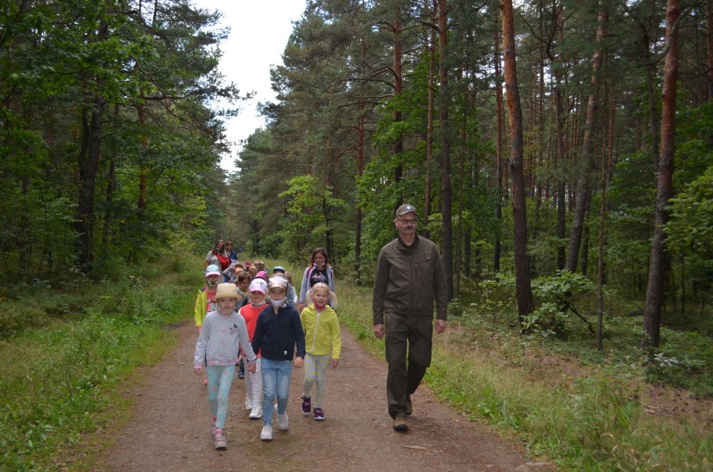 Grupa przedszkolaków wraz z opiekunami i leśniczym idą leśną ścieżką.