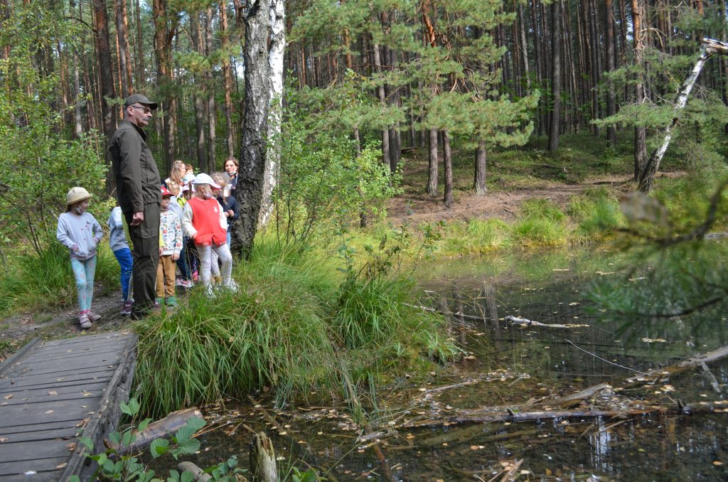 Dzieci wraz z leśniczym i opiekunami obserwują rośliny wodne.