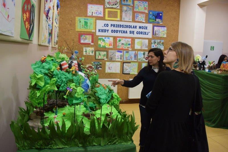 Panie oglądają prace w galerii, jedna ma wyciągniętą rękę pokazuje prace przestrzenne.