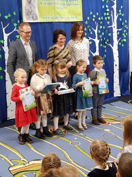 Przed trójką dorosłych stoją nagrodzone dzieci z książkami.