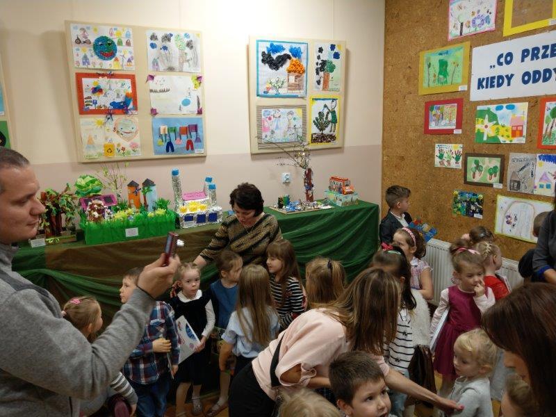 Grupa dzieci ogląda prace w Galerii. Po lewej stronie Rodzic z tel. komórkowym robi zdjęcie.
