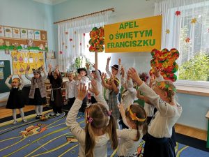 Zdjęcie przedstawia dzieci z grupy Jeżyków śpiewających hymn przedszkola o św. Franciszku i pokazujących gesty do piosenki.