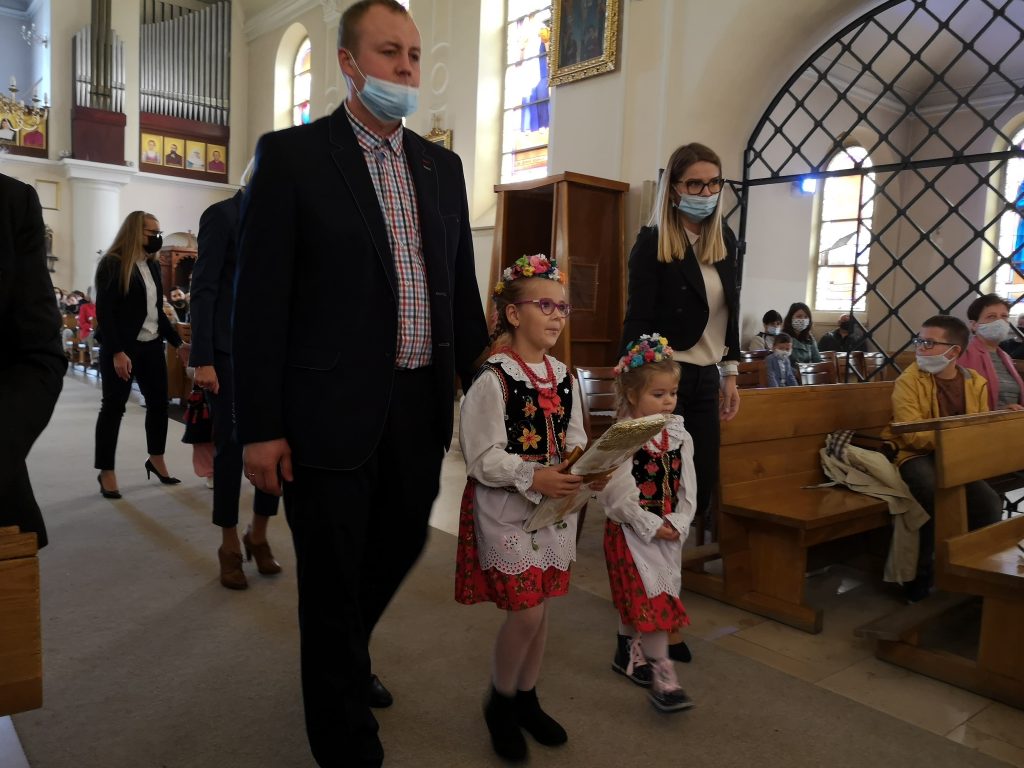 Dziewczynki w strojach krakowskich idą z darem do ołtarza. Za nim idą rodzice.