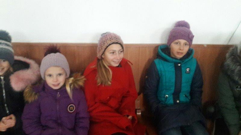 Czwórka dzieciz Ukrainy siedzi pod ścianą na ławce.