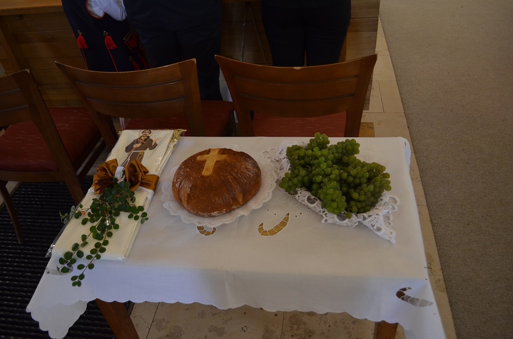 stuła, bochenek chleba i winogrona leżą na stole przykrytym białym obrusie.