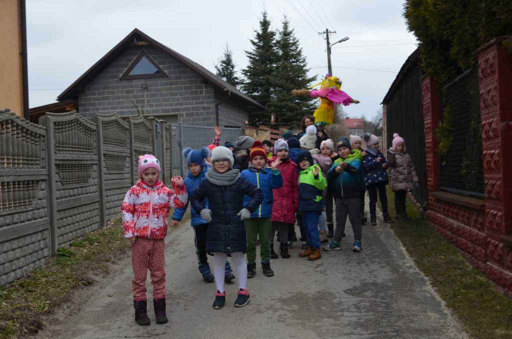 Grupa dzieci z nauczycielem i Marzanną na drodze między domami.
