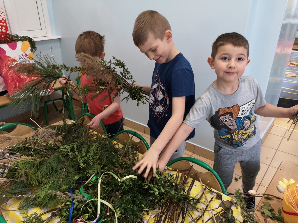 Trzech chłopców tworzy palmy wielkanocne z dostępnych materiałów.