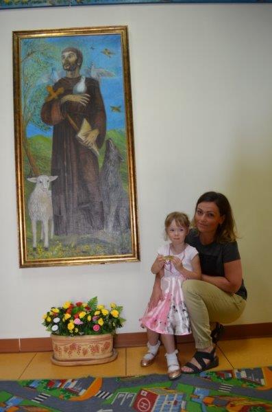 Dziewczynka z nauczycielką w holu z prawej strony obrazu przedstawiającego świętego Franciszka.