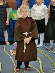 Na pierwszym planie stoi chłopiec przebrany za świętego Franciszka.
