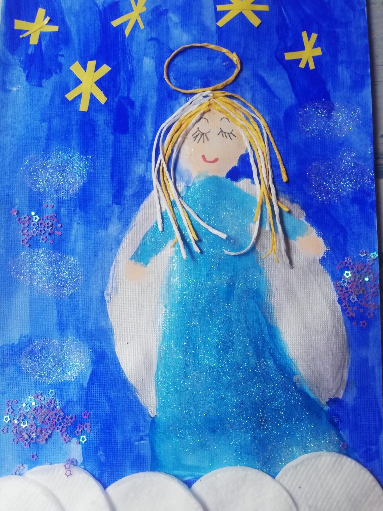 Praca plastyczna przedstawiająca anioła na niebieskim tle.