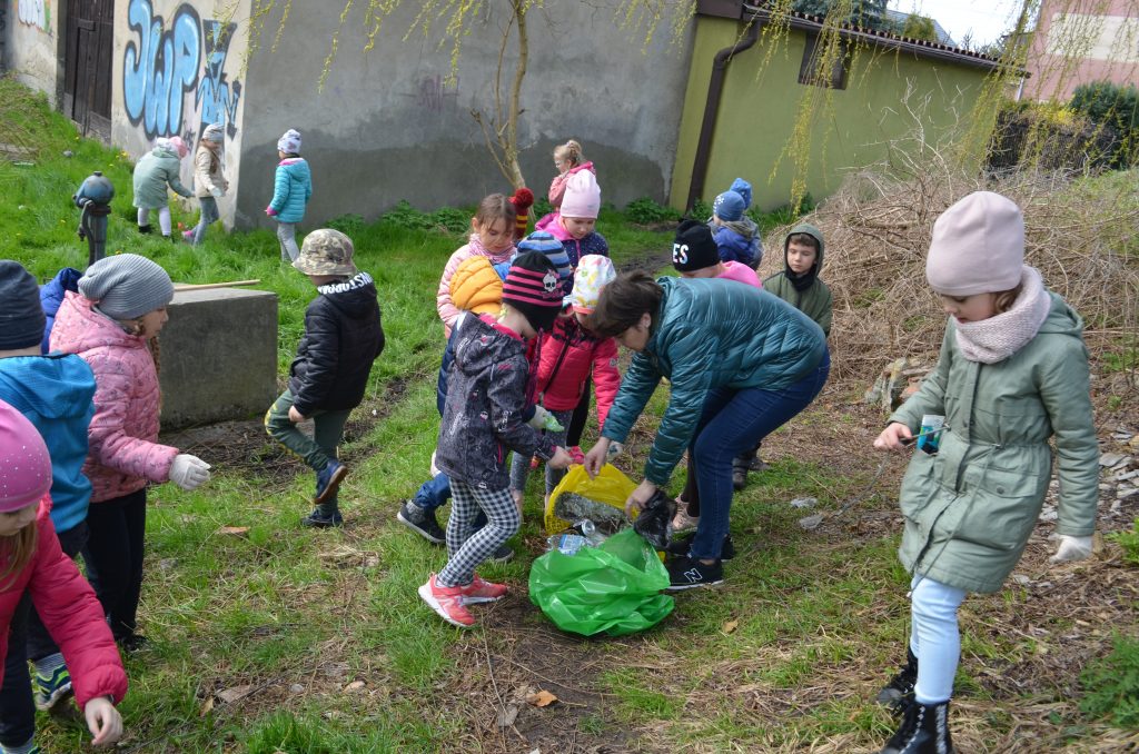 Dzieci zbierają śmieci i wrzucają do zielonego i żółtego worka.
