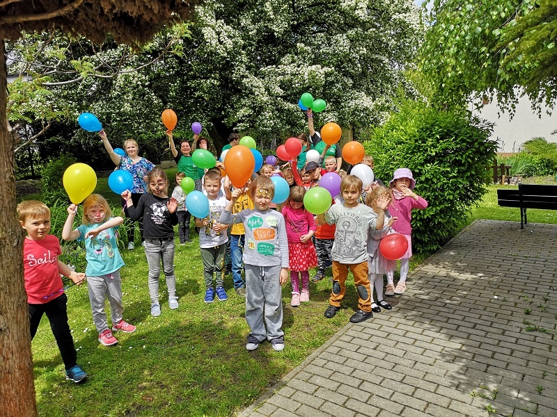 Przedszkolaki z kolorowymi balonami obok oczka wodnego.