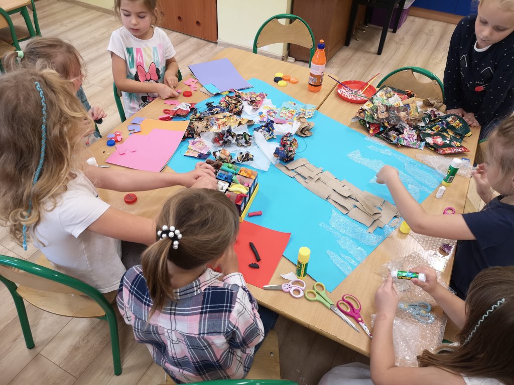Dzieci tworzą pracę plastyczną z materiałów do recyklingu.