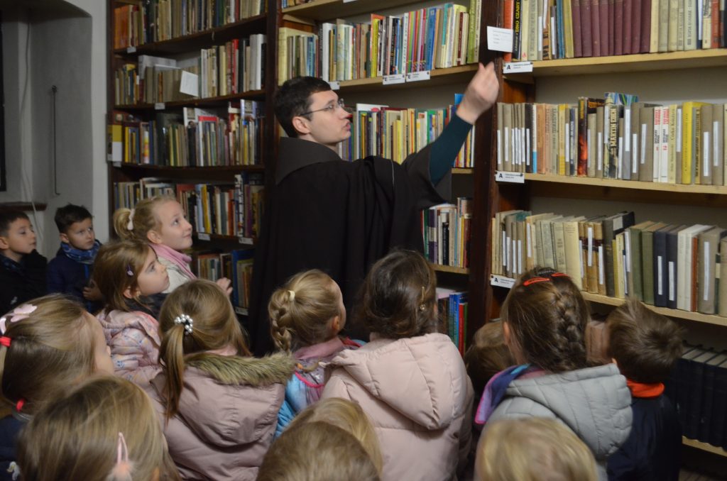 Ojciec Pio pokazuje dzieciom księgozbiory (starodruki) w bibliotece przyklasztornej.