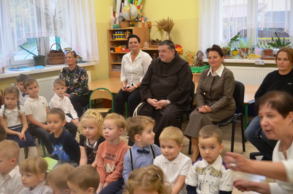 Zdjęcie przedstawia Ojca Lesława, Panią Dyrektor Jolantę Głowacz, pracowników oraz dzieci oglądające występy przedszkolaków.