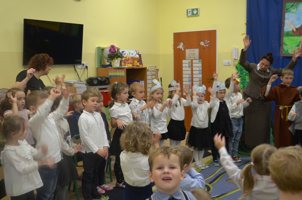 Zdjęcie przedstawia Panią Dyrektor Jolantę Głowacz, pracownika oraz dzieci śpiewające hymn przedszkola.