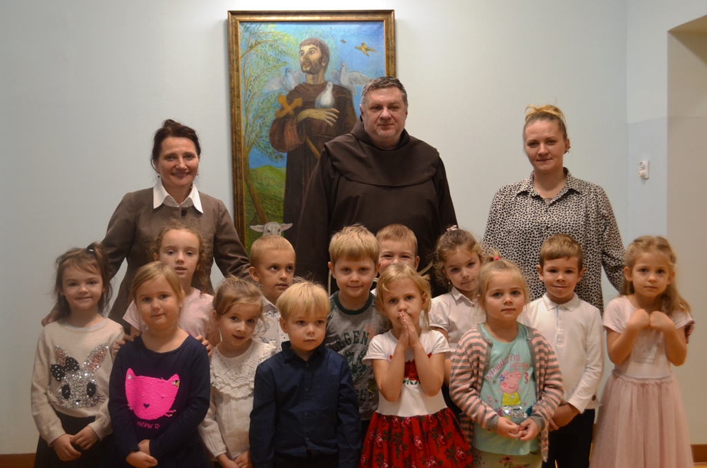 Zdjęcie grupowe przedstawia dzieci z grupy „Jeżyków” wraz z wychowawcą, z Panią Dyrektor Przedszkola Jolantą Głowacz oraz Ojcem Lesławem Zachurą przed obrazem patrona przedszkola – świętego Franciszka.