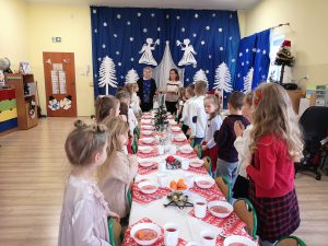 Grupa Biedronki wraz z wychowawcami stoi przy świątecznym stole podczas obchodów Wigilii Przedszkolnej.