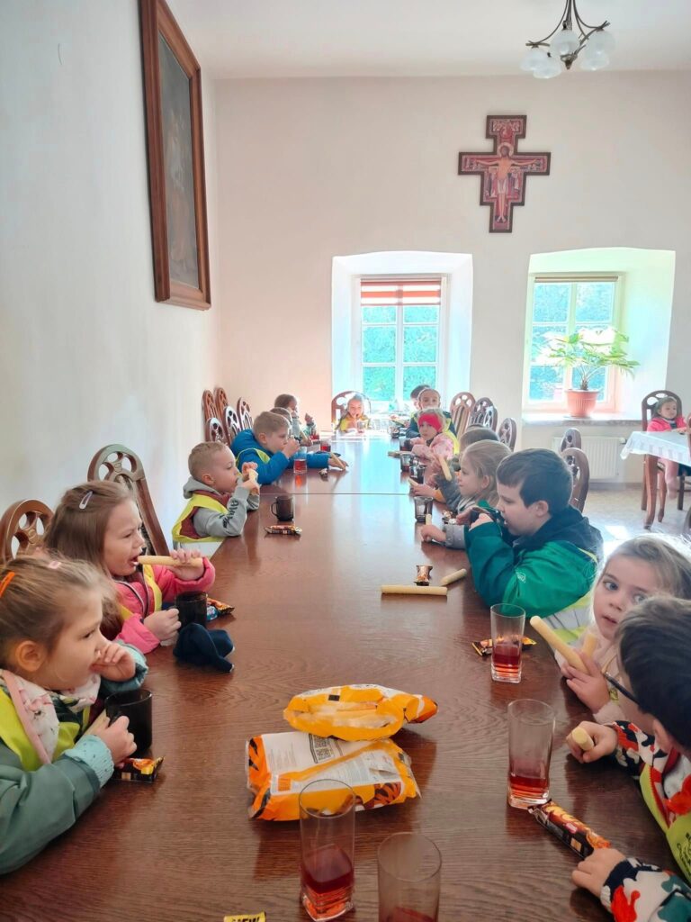Dzieci jedzą słodki poczęstunek otrzymany od zakonnika.
