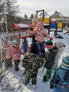 Dzieci stoją przy karmniku i wsypują ziarna dla ptaków.
