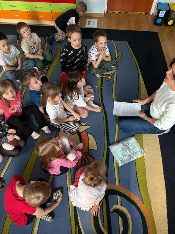 Logopeda prezentuje dzieciom prawidłowy sposób wykonania ćwiczenia buzi.
