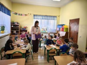 Dzieci siedzą przy stolikach i kolorują.