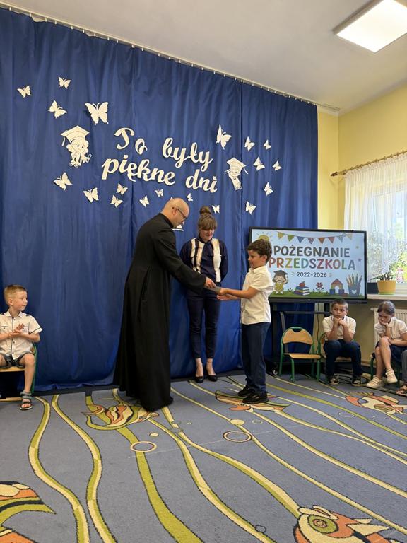 Ksiądz wręcza chłopcu pamiątkowy dyplom.