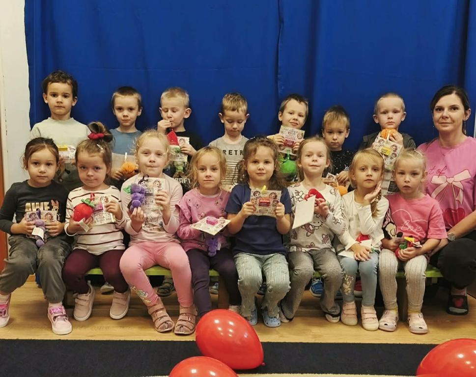 Dzieci z grupy Jeżyki na granatowym tle trzymające w dłoniach drobne upominki z okazji Dnia Przedszkolaka.