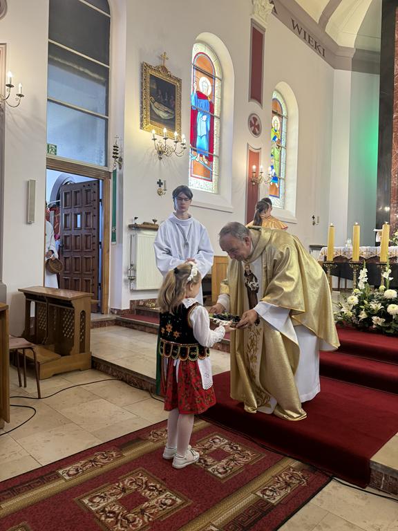 Dziewczynka podaje Księdzu winogrono podczas procesji z darami.
